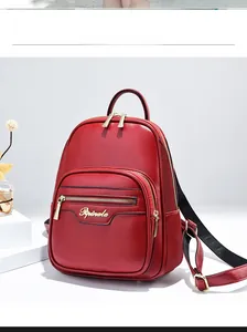 Detail of red faux leather backpack with gold metal logo on a minimalist white stand