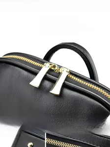 Detail of dual gold zippers, anti-slip base studs, and logo plaque on black leather backpack