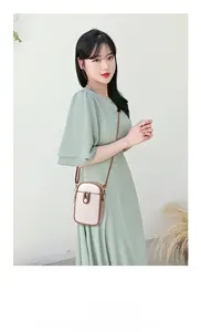 Close-up of elegant cream leather mobile phone bag with brown strap on a green dress