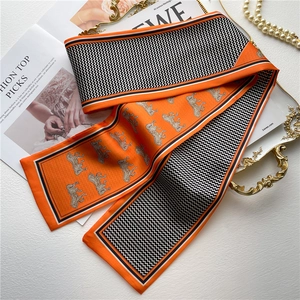 Détail d'une écharpe en soie orange avec motifs équestres et imprimé chevron élégant