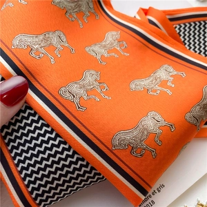 Gros plan du foulard en soie orange avec motif de cheval et bordure en chevron chic