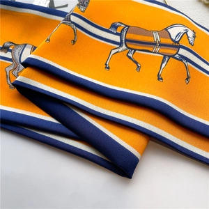 Détail du foulard en soie orange présentant des motifs équestres élégants de chevaux