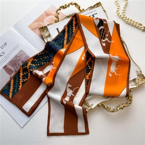 Détail d'un foulard en soie orange et marron avec motif cheval sur plateau doré