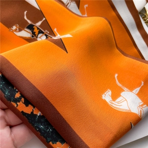 Gros plan détaillé sur un foulard en soie orange avec motifs classiques de calèches