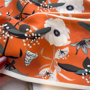 Macro detail of silk floral scarf with orange base, moth print, and delicate ivory rolled edge