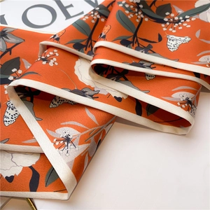 Macro shot of orange floral silk scarf showing fine weave and detailed butterfly print