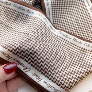 Close-up of brown houndstooth silk scarf detail showing satin texture and logo