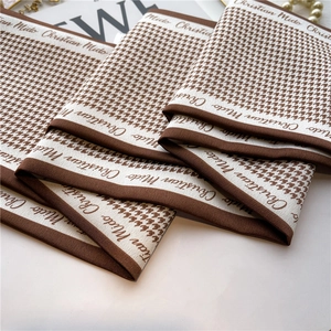 Detailed view of brown and white houndstooth silk scarf with premium edge lettering