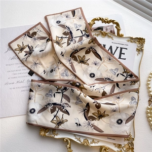 Close-up of floral butterfly print silk skinny scarf on vintage gold embossed tray