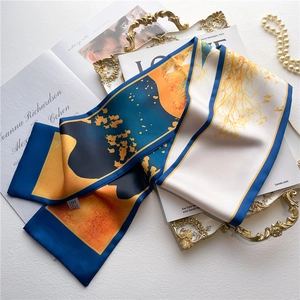 Close-up of silk-feel scarf with navy and orange geometric print on a vintage tray
