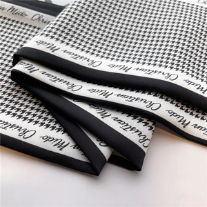 Detail of a black and white houndstooth silk scarf with elegant brand lettering