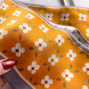 Detail view of the orange and grey silk scarf showing smooth texture and floral pattern