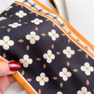 Detail of floral silk scarf showing white flower patterns and orange hem texture