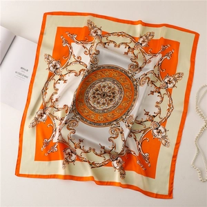 Detailed close-up of orange silk square scarf with golden baroque patterns and pearls