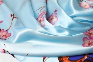 Detailed close-up of sky blue silk scarf featuring pink cherry blossom prints and satin texture