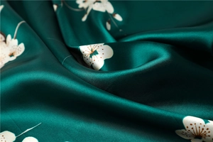 Macro detail of dark green silk scarf with plum blossom pattern and elegant glossy drape