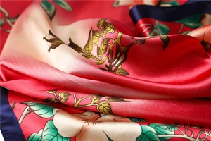 Detail of silk scarf showing elegant floral patterns with smooth satin texture and blue edges