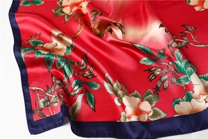 Detail view of red satin silk scarf with floral patterns and contrast blue border
