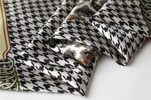 Macro shot of luxury satin scarf featuring black houndstooth and orange paisley patterns