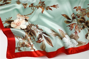 Macro detail of silk satin scarf featuring mint green floral print and red rolled edges