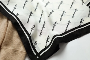 Detail of checkered silk scarf with cursive print and black borders on beige sweater