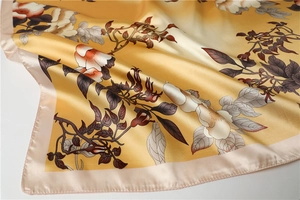 Detailed close-up of golden floral silk scarf showing smooth texture and satin hem