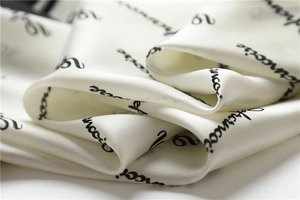 Detailed view of cream silk scarf fabric featuring elegant black cursive text patterns