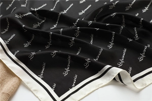 Macro detail of silk-like square scarf featuring elegant black and white letter print patterns