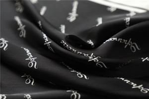 Macro shot of minimalist black silk scarf with white cursive letter patterns and soft texture