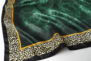 Detail of dark green silk scarf with floral patterns, leopard print edges and satin finish