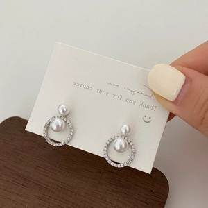 Detail of elegant double pearl earrings with zircon-paved ring held in hand