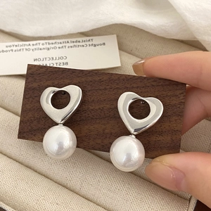 Détail de boucles d'oreilles cœur argenté évidé avec perles blanches sur support bois