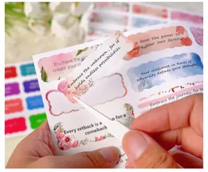 Close-up of watercolor inspirational stickers with floral borders and a white tweezer