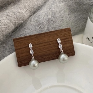 Détail de boucles d'oreilles longues en perles et zircons sur un présentoir en bois