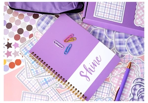 Macro detail of purple spiral notebook with Shine text and matching stationery accessories