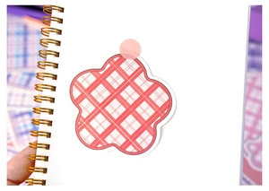 Close-up of pink checkered flower sticker on a white spiral notebook page for journaling
