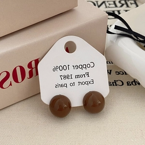 Detailed close-up of brown enamel spherical stud earrings on a white display card