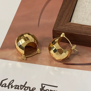 Vue macro de boucles d'oreilles dorées avec surfaces facettées et finition métallique