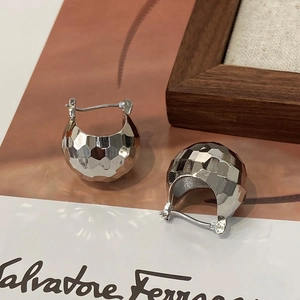 Gros plan sur des boucles d'oreilles boules argentées aux facettes géométriques sur bois