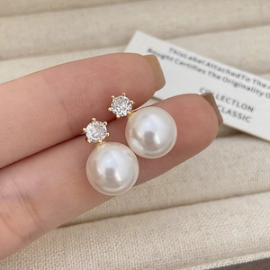 Macro shot of minimalist pearl earrings with zircon inlay held by hand for detail