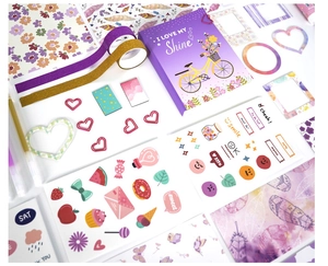 Flat lay of purple themed scrapbook kit featuring stickers, tapes, and stationery items
