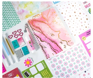 Flat lay of pink marble spiral notebook with assorted pens and decorative stickers