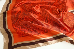 Detailed close-up of orange silk scarf with classic paisley patterns and striped borders