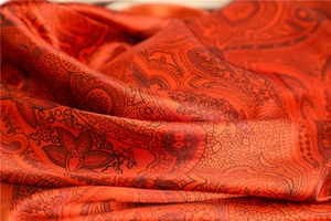Macro view of orange silk scarf featuring vintage paisley patterns and floral textures