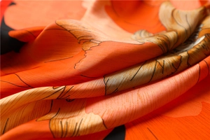 Gros plan sur un foulard en soie orange avec motif pivoine et texture lisse soyeuse