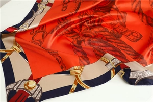 Detail of silk square scarf featuring orange equestrian pattern and belt buckle design