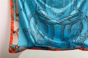 Detailed view of silk scarf featuring royal blue equestrian print and orange edges