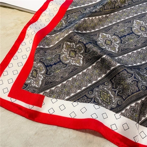 Detail of silk-feel scarf with vintage paisley patterns and vibrant red border on plush background