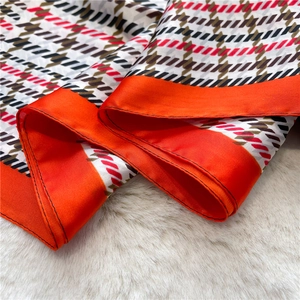 Detailed view of the houndstooth pattern and vibrant orange border on the silk scarf