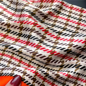 Detail of houndstooth pattern scarf fabric showing silky texture and vibrant red hem